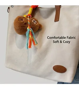 Detail of cream canvas tote bag with brown leather handles and a plush bear keychain