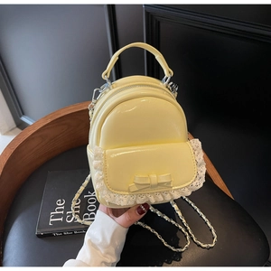 Close-up of yellow patent leather mini backpack with lace trim and bow detail