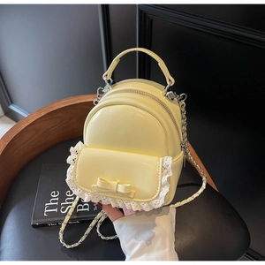 Detail of light yellow mini backpack with lace ruffles, bow decoration, and chain strap