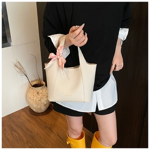 Detail of off-white lychee leather bucket bag with pink satin bow and embossed logo