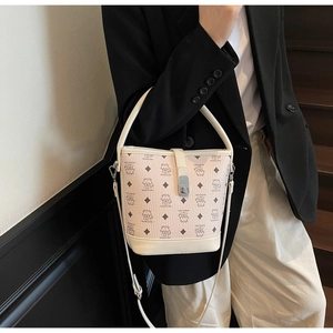 Detail of cream white leather bucket bag with cat pattern and brand logo carried by a model