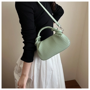 Detail of mint green pleated handbag with knot handle and detachable strap on model