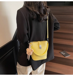Detail of yellow bucket bag with plush bear charm worn by a model in a black suit