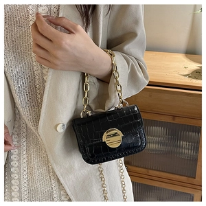 Detail of a black faux crocodile skin girls bag featuring a gold disc lock and chain straps