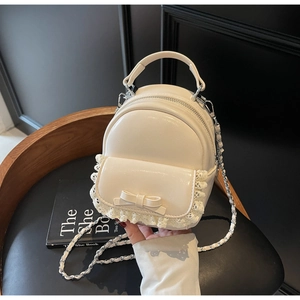 Detail of a beige mini backpack with sweet bow and lace trim featuring a metal chain strap