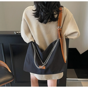 Detail of the large black tote bag featuring silver chain decor and brown leather straps