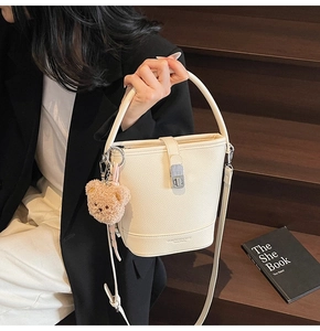 Detail of cream white bucket bag with pebble texture, silver buckle and plush bear charm