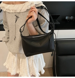 Detail of black lychee grain leather shoulder bag with side knot and zipper on model