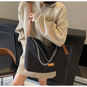 Detail of black nylon tote bag featuring silver chain decor and brown leather strap