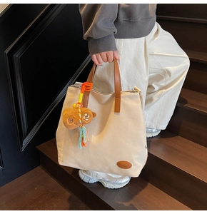 Detail of canvas tote bag featuring leather logo, plush bear charm and woven tassels