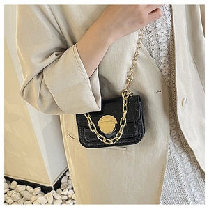 Detail of a black crocodile-texture girl crossbody bag with large gold lock and chain
