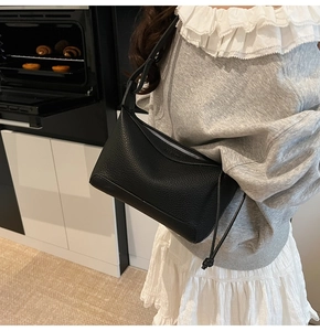 Close-up of black lychee grain leather handbag with silver zipper and knot detail