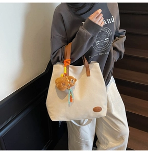 Detail view of canvas tote bag featuring brown leather logo patch and plush bear accessory