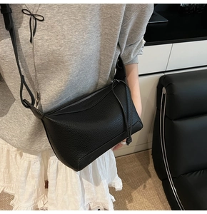 Detail of black crossbody bag with lychee texture and decorative knotted shoulder strap