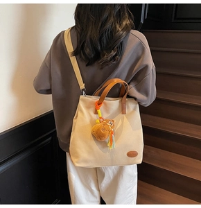 Detail of canvas tote bag featuring brown leather handles and a cute plush bear charm