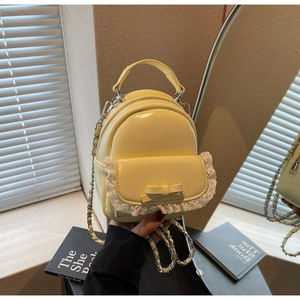 Detail of a creamy yellow mini backpack with lace trim, bow, and a golden chain strap