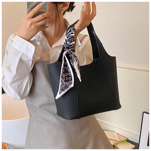 Detail of a black pebbled leather bucket bag with a black and white heart print silk scarf
