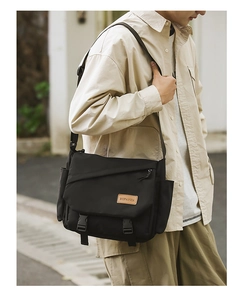 Detail of black nylon messenger bag featuring leather brand tag and buckle closure