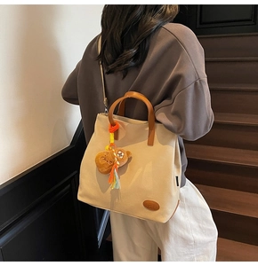 Detail of beige canvas tote with brown leather handles and cute plush bear charm