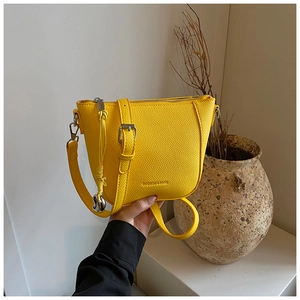 Détail du sac seau jaune en cuir grainé avec pendentif tressé et bandoulière réglable