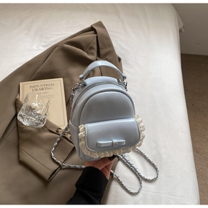 Detail of light blue mini backpack with white lace trim and elegant leather bow accent