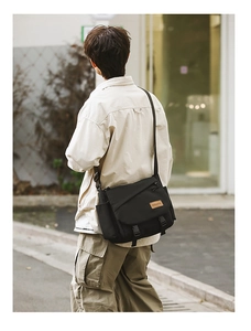 Detailed view of black canvas messenger bag featuring adjustable strap and logo patch