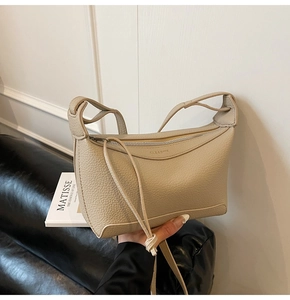 Close-up of beige lychee grain leather crossbody bag with zipper and logo detail