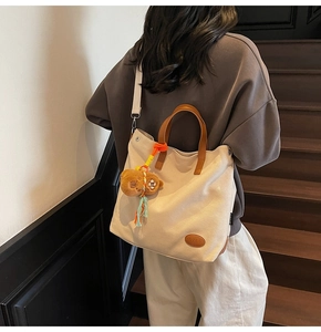 Detail of canvas tote bag featuring brown leather handles and cute bear plush charm