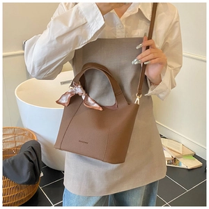 Detail of a brown lychee pattern leather bucket bag with decorative silk scarf accessory