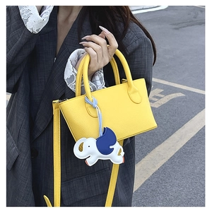 Close-up of bright yellow leather bucket bag with cute elephant charm on a stylish model