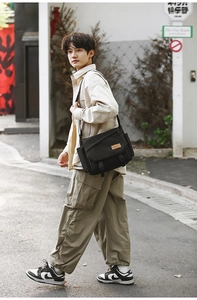 Detail of black canvas messenger bag with dual buckles and leather logo in street setting