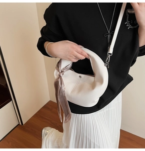 Detail der cremeweißen Handgelenktasche aus genarbtem Leder mit dekorativem Seidenschal-Griff