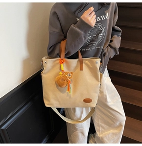 Detail of beige canvas tote with brown leather handles and cute plush bear charm decoration