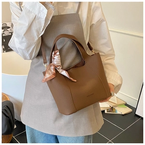 Detail view of brown pebbled leather bucket bag with a pink decorative silk scarf on the handle