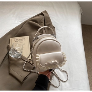 Detailed close-up of cream mini backpack with lace trim and bow accent held by hand