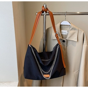 Detail of a large black tote bag with brown leather straps and silver metal chains