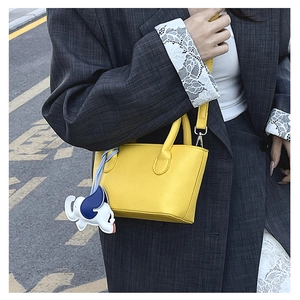 Detail of yellow lychee leather bucket bag with a blue elephant charm pendant