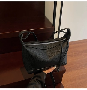Close-up of black lychee grain leather crossbody bag on a wooden staircase background