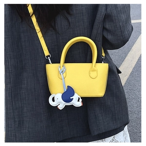Detail of a bright yellow mini tote bag with elephant charm on a model in a grey suit