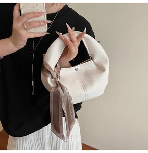 Detail der weißen Handtasche mit Lychee-Struktur, geometrischem Seidentuch und Silberbeschlag