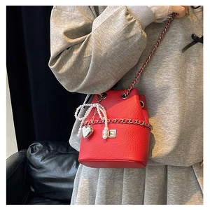Detail of red bucket bag with litchi texture, metal chain and pearl bow pendant decoration