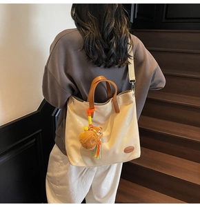 Detailed view of canvas tote bag with brown leather handles and plush bear charm