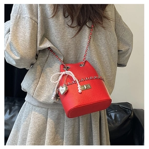 Detail of red bucket bag with pearl bow and silver chain worn on grey casual suit