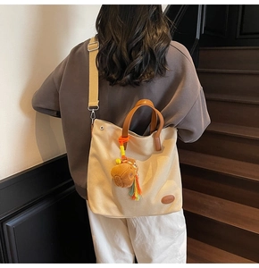 Detail of beige canvas tote bag with brown leather handles and orange horse charm