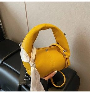 Detail der gelben Lederhandtasche mit klobigem Griff und elegantem weißen Seidentuch-Dekor