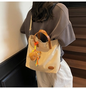 Detail view of beige canvas tote with brown leather straps and small bear charm