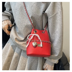 Detail of red quilted bucket bag with pearl bow and heart charm on silver chain strap