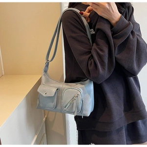 Detail of light blue glossy leather shoulder bag with utility pockets and metal buckle