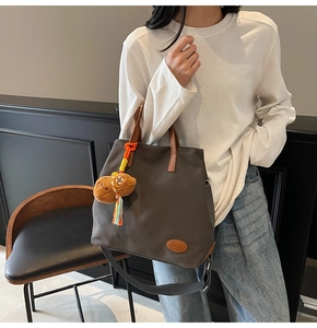 Detail of canvas tote bag featuring brown leather handles and a plush bear pendant