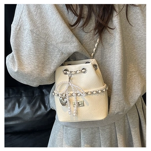 Close-up of beige quilted bucket bag with pearl bow, metal chain strap and heart charm